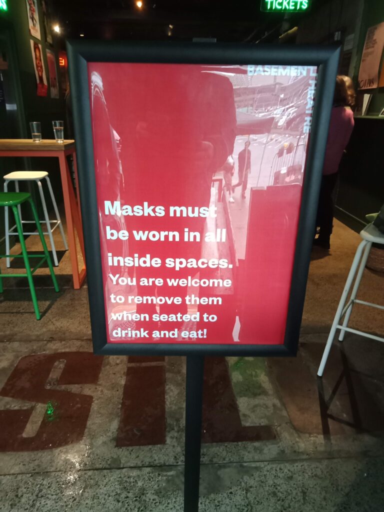 The sign reads: "Masks must be worn in all inside spaces. You are welcome to remove them when seated to drink and eat!"
